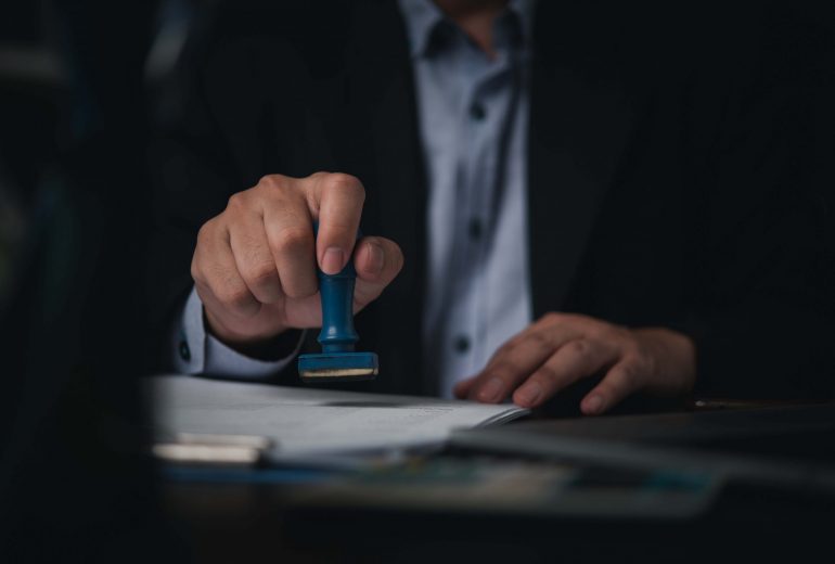 Hand man stamping documents notary public in office . Businessperson stamping approval of work finance banking or investment marketing documents on desk.